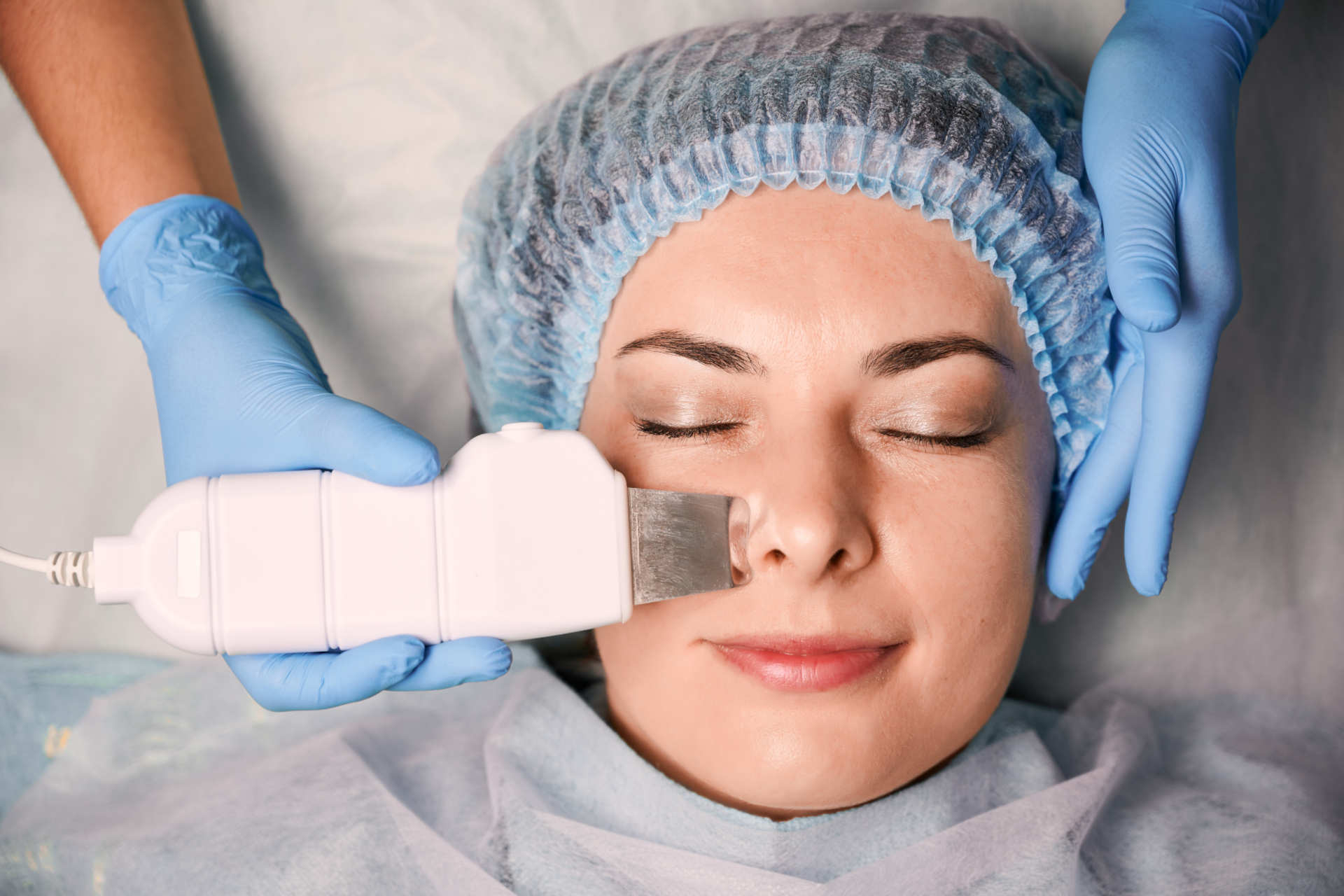 Cosmetologist cleaning woman forehead with ultrasonic scrubber.